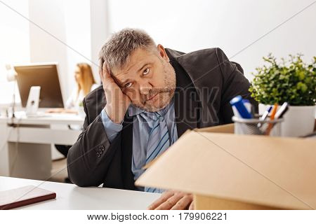 Awful situation. Overwhelmed sorrowful pudgy man sitting at his desk and thinking about what he doing wrong in his work