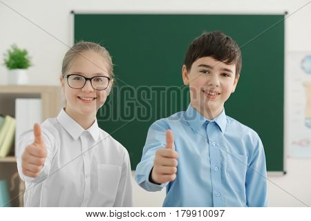 Cute boy and girl standing near green school blackboard in classroom