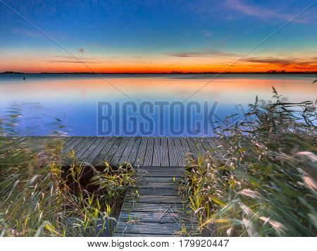 Long Exposure Image Of Blue And Orange Sunset Over Boardwalk On The Shore Of A Lake
