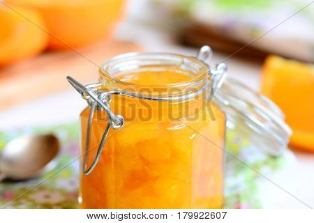 Home orange jam. Sweet orange jam in a glass jar, spoon, textile, napkin, orange slices on a table. Easy citrus dessert. Closeup