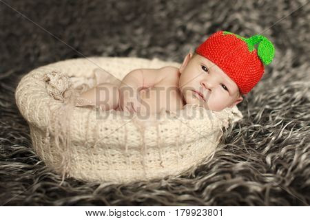 Newborn baby sleeping on fur in the basket in funny hat like berry or tomato