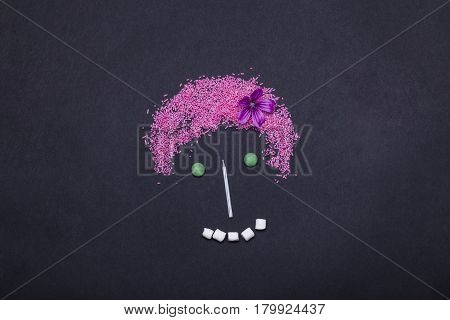 pink sprinkles sweets dragee marshmallow zephyr and birthday cake candle in shape of human girl face or smiley on grey background