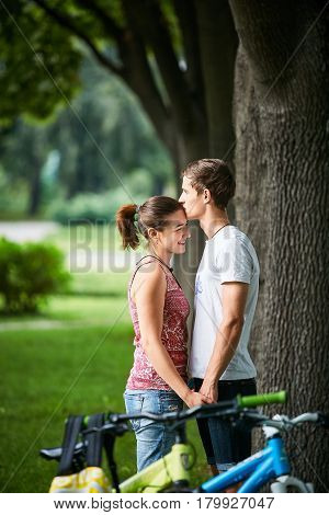 Young people, couple with bicycles in the park. A loving couple on a date on a summer evening. The guy with the girl hugs and kisses. Youth, first feelings, first love, first dates