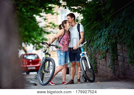 Young people, couple with bicycles in the park. A loving couple on a date on a summer evening. The guy with the girl hugs and kisses. Youth, first feelings, first love, first dates