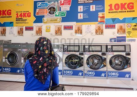 Labuan,Malaysia-Apr 3,2017:Muslim girl waiting the laundry into coin-operated washing machines at laundromats self operated laundry in Labuan,Malaysia on 3rd April 2017.