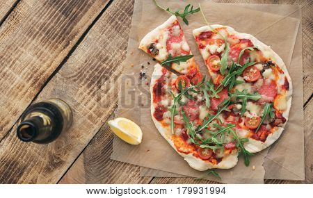 Pizza with salami cherry tomato mushrooms and arugula on wooden table with beer top view with copy space