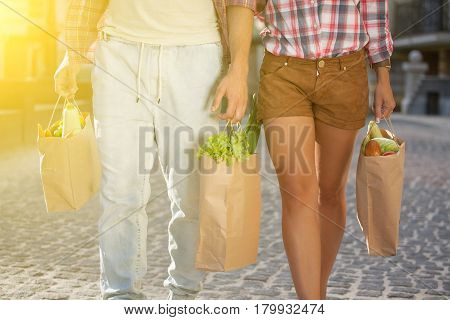 Toned image. Young man and woman goint to home after shopping. Beautiful couple praparing for picnic with their frind in the park.