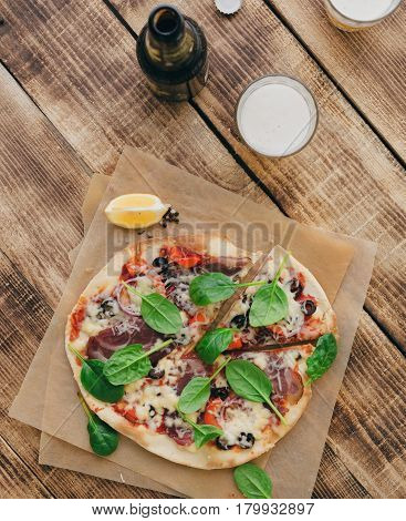 Pizza with meat pepper olives onion and spinach with a light beer on a wooden table top view