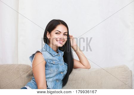 Relaxed casual brunette in blue cardigan and In blue jeans sits on the couch in bright living room