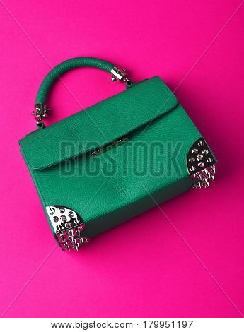 Nice beautiful small womans leather green fashionable bag with decorative metallic spikes or thorns on pink background