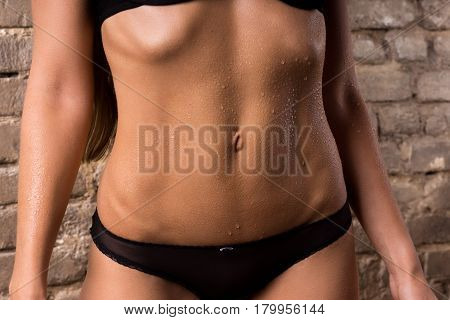 Female slender belly аgainst a brick wall background.