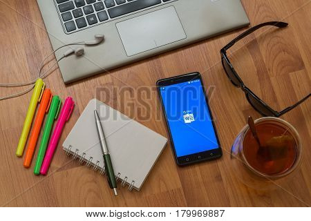 Nitra, Slovakia, april 3, 2017: Microsoft office word application in a mobile phone screen. Workplace with a laptop, an earphones, notepad, pen, tea, sunglasses and color markers on wooden background