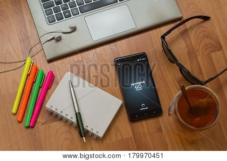 Nitra, Slovakia, april 3, 2017: TomTom Go application in a mobile phone screen. Workplace with a laptop, an earphones, notepad, pen, tea, sunglasses and color markers on wooden background