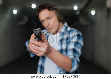 Prepared to shoot. Nice brutal professional marksman holding a handgun and aiming with it while training how to shoot