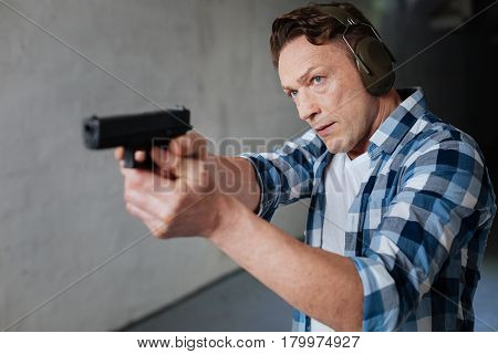 Favourite activity. Nice handsome pleasant man holding a handgun and aiming at the target while visiting the shooting range