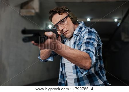 One shot. Confident skilled nice shooter holding the gun and pulling the trigger while shooting