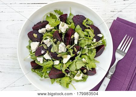 Beetroot salad, top view, on grunge white timber.  Arugula, feta cheese, and pepitas.