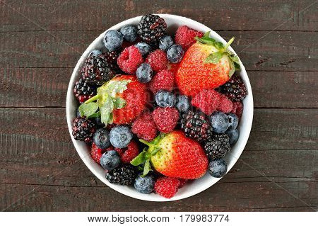 Mix of strawberries, blueberries, blackberries and raspberries fruit on wood table. Forest fruit in white idaeus. Delicious fresh berries.