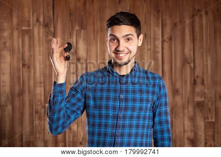 Man in plaid shirt holds car keys on brown background