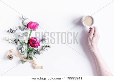 Modern spring design with bright pink flowers and coffee in hand on white desk background top view moke up