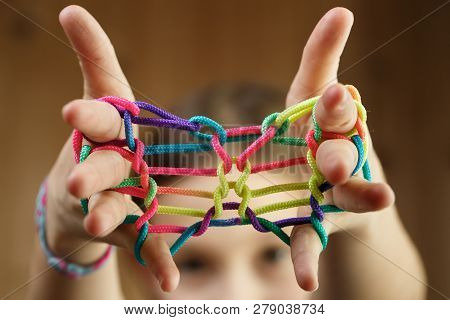 Child playing classic, old-school string game and didactic toy with her fingers, creating shapes, developing her motor skills. IQ, education, intelligence, fun and childhood concept.