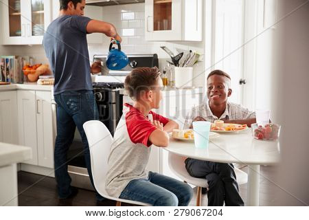 Two pre-teen male friends sit talking in kitchen at one boyÃâ¢s house, dad in the background