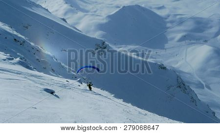 Paraglider Starts Flying In The Mountains, Skiing On A Slope Against The Background Of A Small Rainb