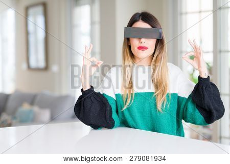 Young beautiful woman blindfold eyes with black censor band at home relax and smiling with eyes closed doing meditation gesture with fingers. Yoga concept.