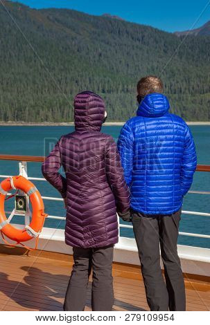 Couple In Colorful Purple And Blue Winter Puffer Jackets View Alaska, Usa Coastl From Ships Deck On 
