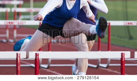 High Achool Girls Running In A Hurdle Race Outside During A Spring Track Snd Field Race.