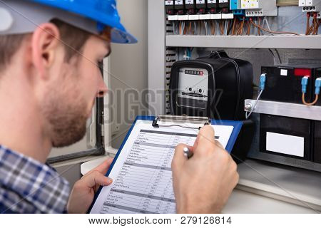Close-up Of Male Technician Writing On Clipboard In Front Of Fuse Box