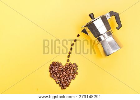 Coffee Beans Pouring From Coffee Maker Into A Heart Shape On Yellow Background. Love Coffee Concept.