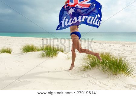 Woman In Bikini Running Along Beach Holding A Billowing Australian Flag.  Australia Day Celebrations