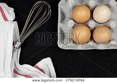 Top View Of Hen Eggs In A Carton Box And An Eggbeater On A Black Background.