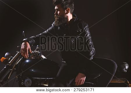 Brutality And Masculine Concept. Man With Beard, Biker In Leather Jacket Lean On Motor Bike In Darkn
