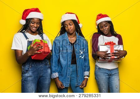 Three African Woman In Santa Hat Share Christmas Present On Yellow Background