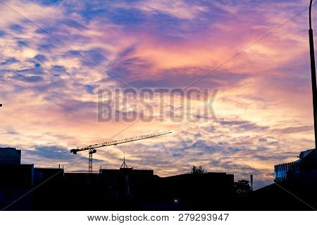 Urban Skyiline In Silhouette With Heavy Colorful Clouds Overhead And Construction Crane Above Buildi