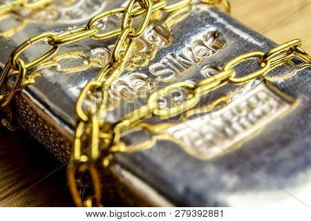 Closeup Of Silver Brick In Golden Chains Laying On Wooden Background