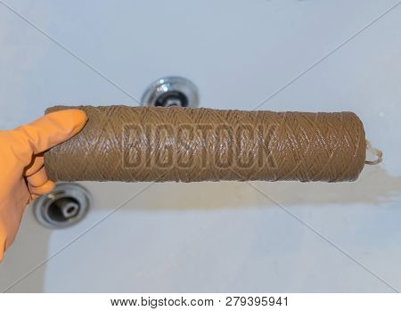 Hand Holding Dirty Water Filter Cartridge Over The Bathhub