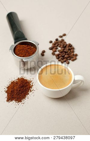 Cup Of Black Coffee Next To Coffee Beans And Grains, Handle Coffee Machine Filter On Gray Background