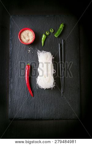 Asia Food - Rice Noodles, Spicy Pepper, Sticks And Sesam, Ready To Cook On A Dark Stone Background, 