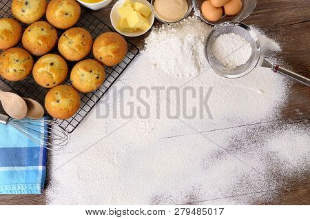 Baking Background With Dusted Flour On A Dark Wood Table With Freshly Baked Muffins And Ingredients.