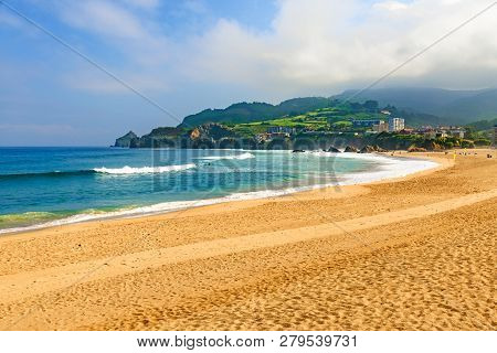 View Of Sandy Beach In Bakio, Basque Country, Spain With Waves And Surfers