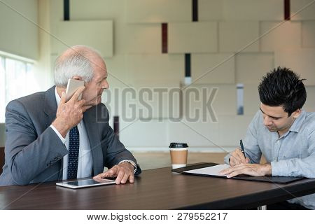 Businessman Filling Document At Meeting. Senior Entrepreneur Talking On Phone When His Colleague Tak