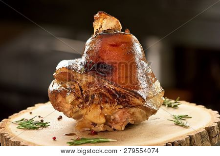 Roasted Piece Of Meat On Table. Roasted Pork Leg On Wooden Stamp With Gerb And Cranberry.