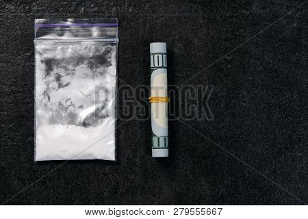 Rolled Hundred Dollars Banknote And Plastic Packet Of Cocaine On Black Background, Copyspace
