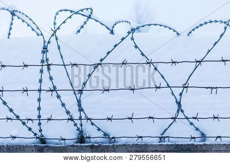 The Barbed Wire Silhouette On The Background Of Snow And Blue Sky