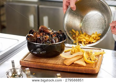 Pouring Out French Fries From Sausepan. Mussels With Side Dish.