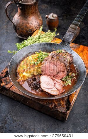 Barbecue roast boar joint with roesti and game red wine sauce as top view in a wrought-iron pan