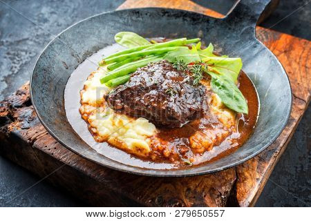 Traditional German braised veal cheeks in brown sauce with mashed potatoes and beans as closeup in a wrought-iron pan